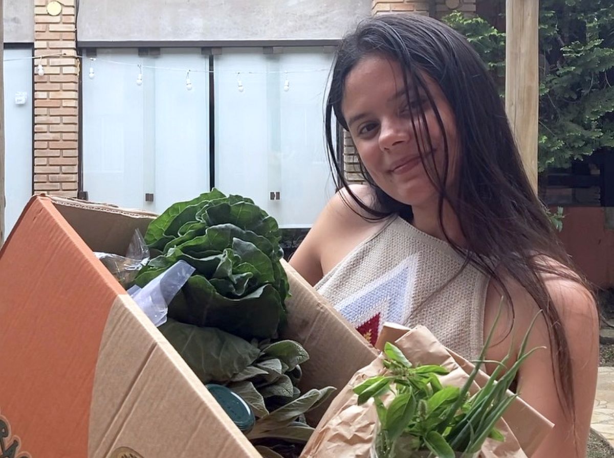 Jovem aparece na feira segurando uam caixa com várias verduras e legumes