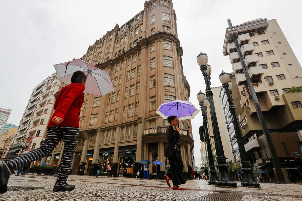 Imagem mostra pessoas andando no Centro de Curitiba com guarda chuva.