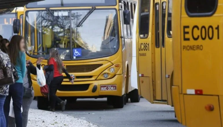 Na imagem, ônibus do sistema de transporte coletivo de Curitiba e pessoas aguardando no ponto para embarcar.