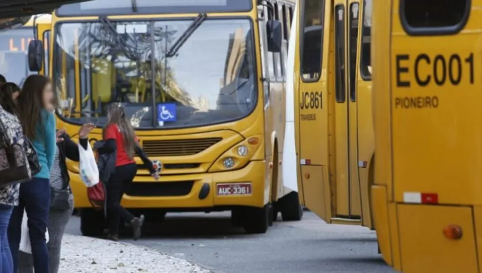 Na imagem, ônibus do sistema de transporte coletivo de Curitiba e pessoas aguardando no ponto para embarcar.