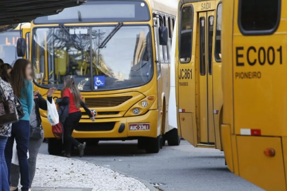 Na imagem, ônibus do sistema de transporte coletivo de Curitiba e pessoas aguardando no ponto para embarcar.