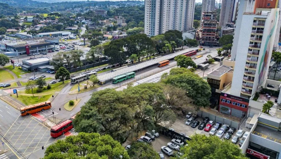 Imagem aérea mostra o novo smart park de Curitiba. A imagem de prédios, um terminal com ônibus e muitas árvores.