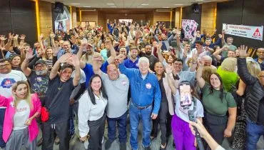 Imagem mostra quase uma centenas de pessoas no salão onde foi realizada a convenção. No centro, Requião de braça direito erguido posando para a foto com correligionários ao redor