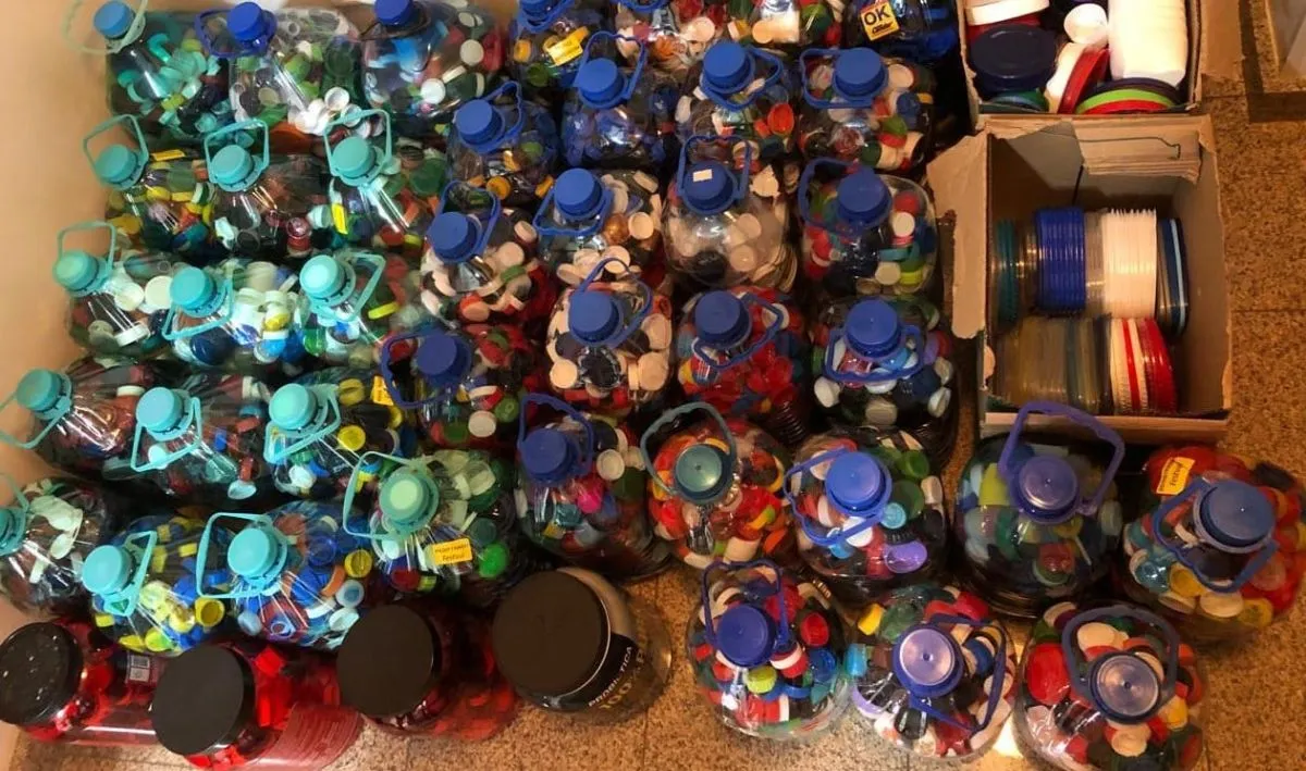 Imagem mostra pelo menos uma dezena de garrafas de 5 litros de água cheias de tampinhas de plástico de refrigerantes e outros potes.