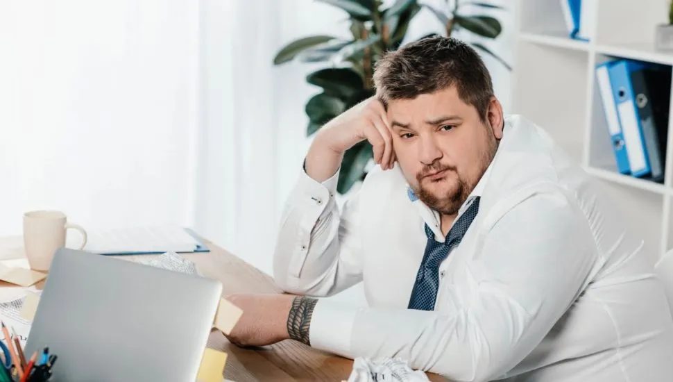 Imagem mostra homem obeso, de terno, sentado com cara de frustrado