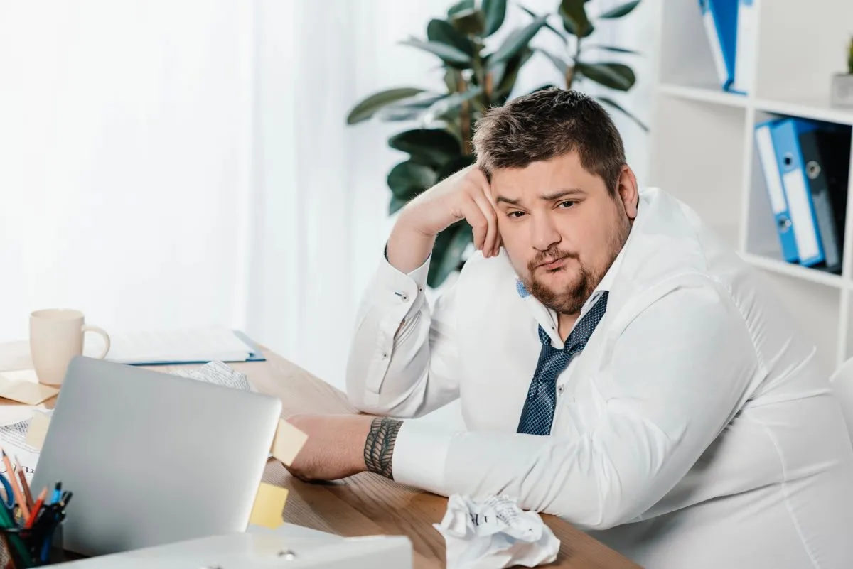 Imagem mostra homem obeso, de terno, sentado com cara de frustrado