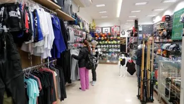 Imagem mostra in interior de uma loja tradicional de Curitiba, com roupas em uma arara e clientes passeando. AO lado, itens esportivos como bolas, tacos e mais.