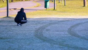 Imagem mostra geada no Parque Barigui, em Curitiba, Com pessoas andando no gramado branco de gelo.