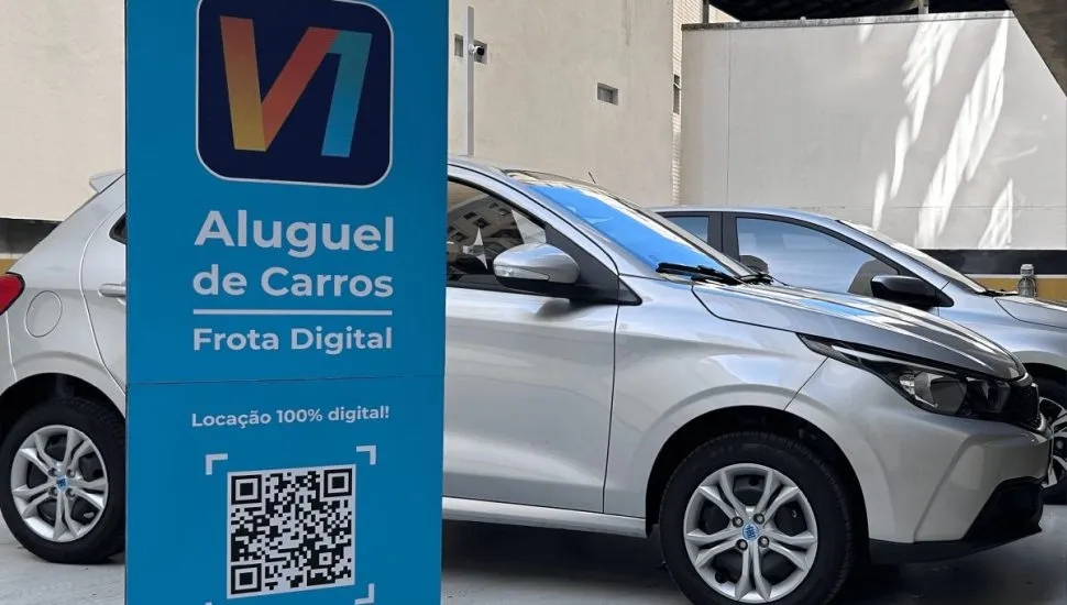 Foto mostra um dos carros da empresa, atrás de um totem com a marca da startup e um QR Code que libera o aluguel do carro