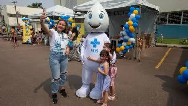 Imagem mostra o personagem Zé Gotinha, que simboliza a gotinha da vacina contra a polio. Ele está posando para fotos junto com crianças