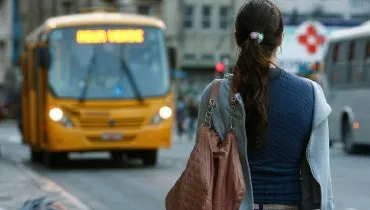 Jovem espera para embarcar em ônibus em ponto em rua de Curitiba.