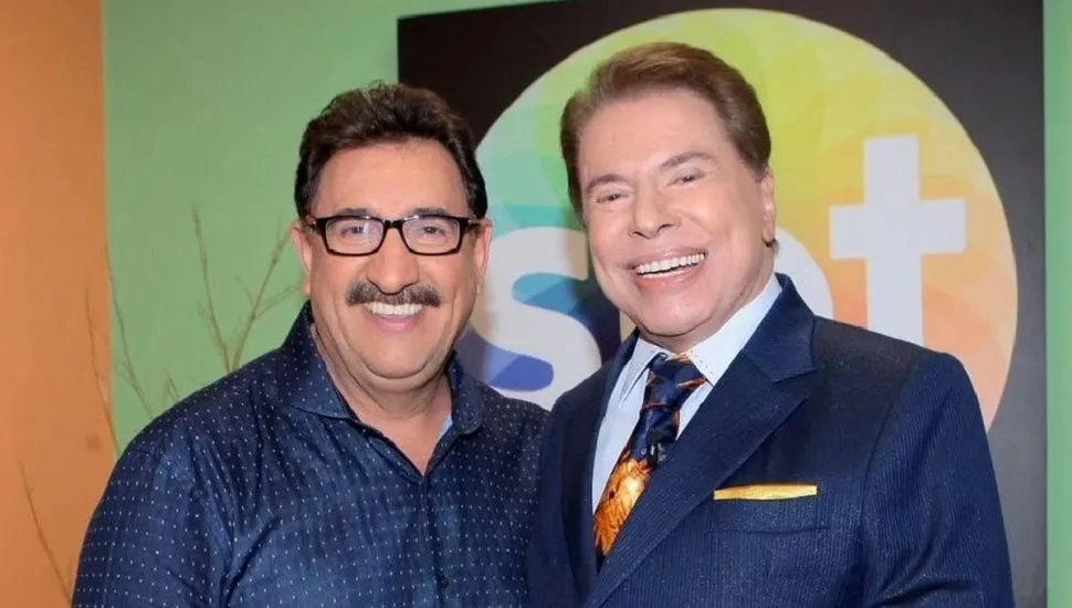 foto mostra o apresentador ratinho posando ao lado de Silvio Santos, com a logo do SBT ao fundo