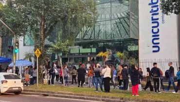 Imagem mostra concurseiros em frente a um local de prova em Curitiba. São diversas pessoas em fila na frente da UniCuritiba. Tem um carro branco e pessoas na foto.