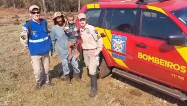 Imagem mostra uma equipe do Corpo de Bombeiros com uma criança nos braços. A foto tem uma viatura vermelha.