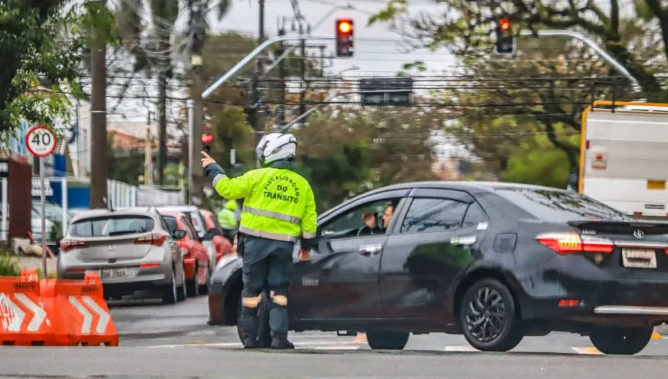 Motorista é orientado por agente de trânsito em rua com bloqueio.