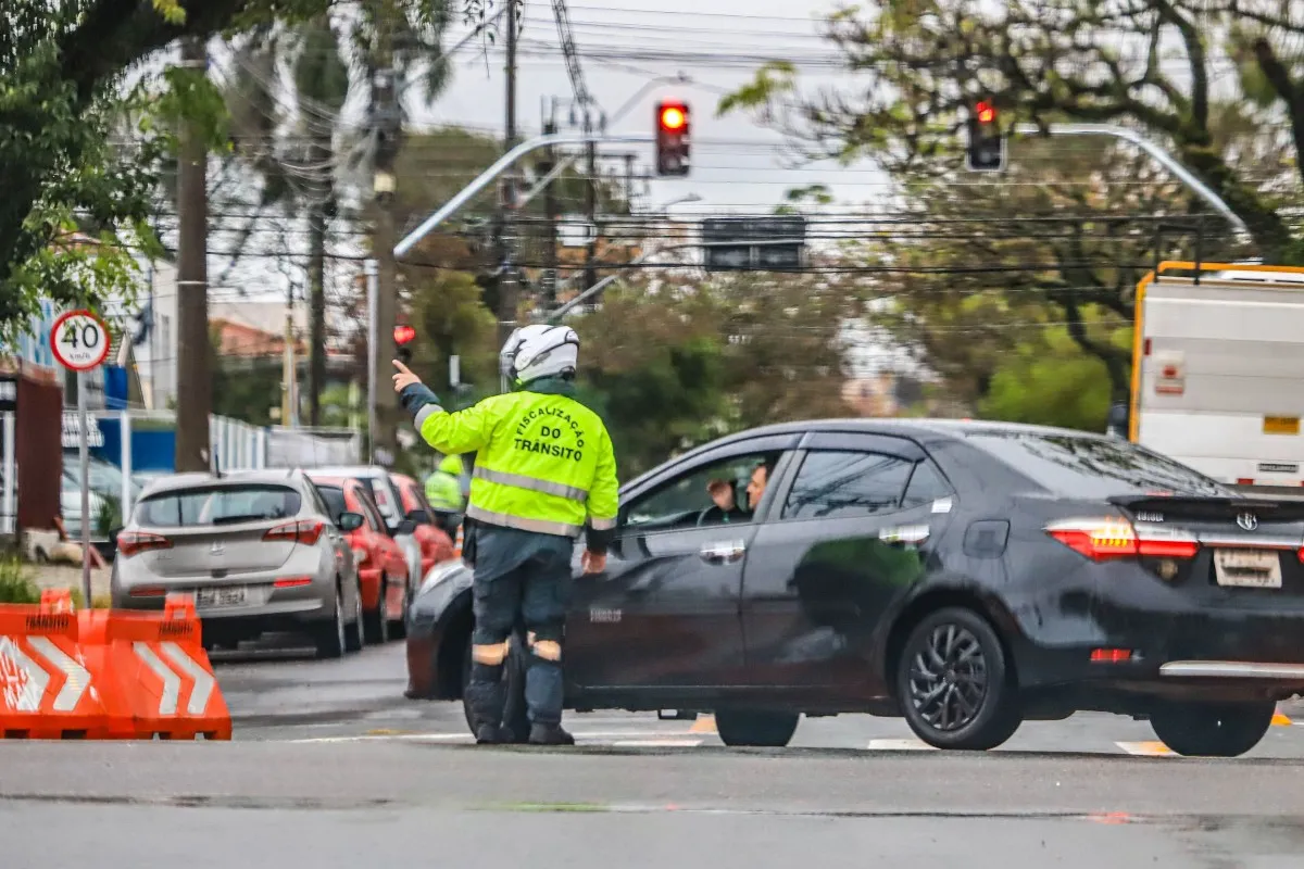 Motorista é orientado por agente de trânsito em rua com bloqueio.