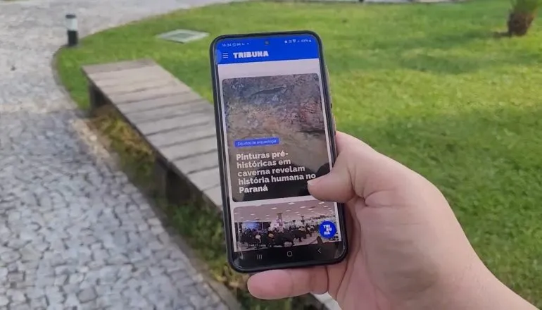 Homem segurando smartphone com o site da Tribuna do Paraná.