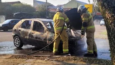 Imagem mostra um carro incendiado em uma rua de Curitiba com bombeiros abrindo o capô.