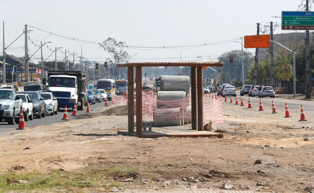 Imagem mostra um ponto de ônibus entre duas pistas de uma avenida com cones e congestionamento.