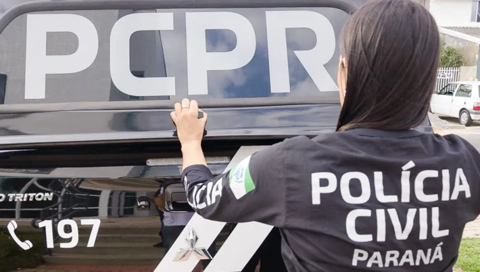 Imagem mostra uma policial civil de costas fechando um camburão.