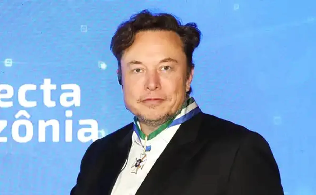 Imagem mostra Elon Musk com o cabelo bagunçado e em um fundo azul.