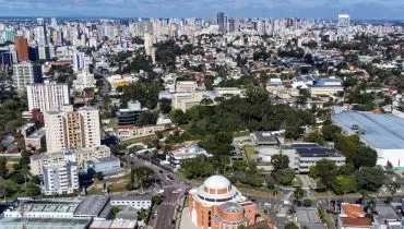 Imagem mostra Curitiba vista de cima, com muitas árvores e prédios baixos.