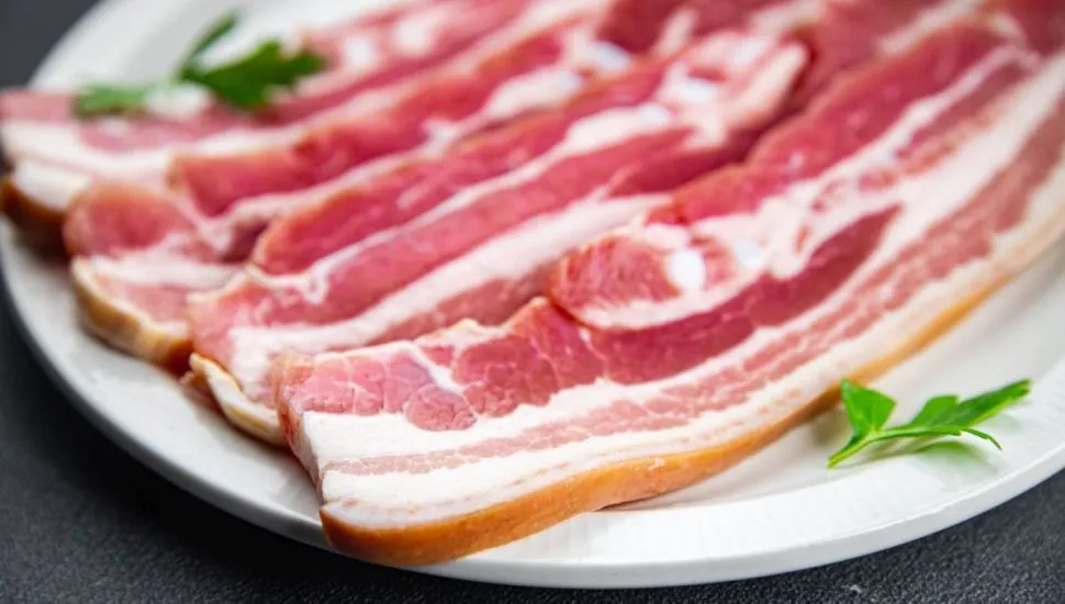 imagem mostra quatro fatias de bacon cru em um prato decorado com ervas