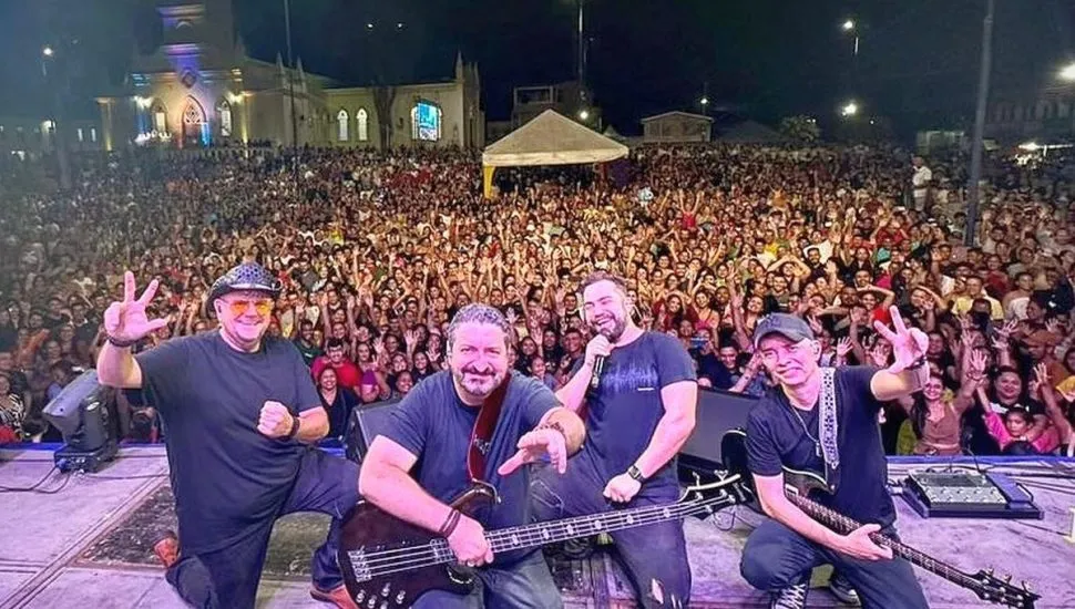 imagem mostra integrantes da banda no palco de um show, com o público ao fundo