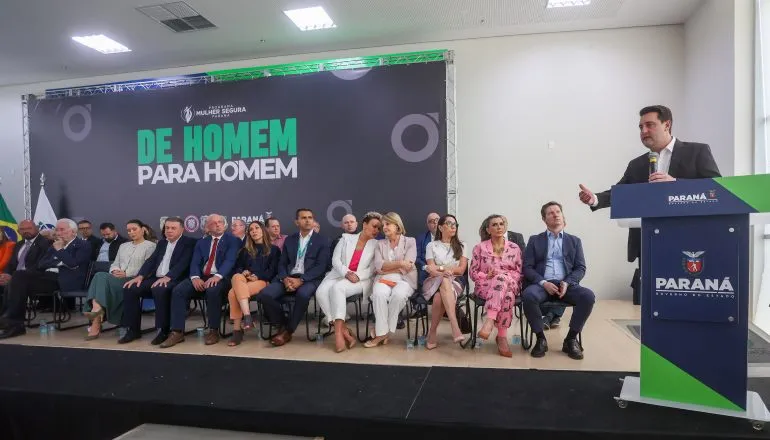 Na imagem, foto do palco do evento "De Homem para Homem", com várias autoridades e convidados. Governador fala no púlpito. 