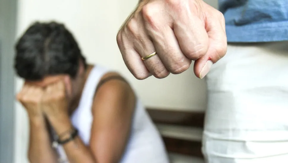 Na imagem, uma mulher aparece ao fundo, acuada e cobrindo os olhos. E também há um homem com a mão fechada, em uma simulação de violência contra a mulher.