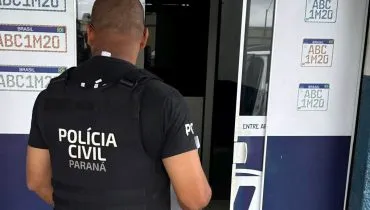 Na imagem, policial em frente à porta de entrada de uma empresa de emplacamento de veículos.