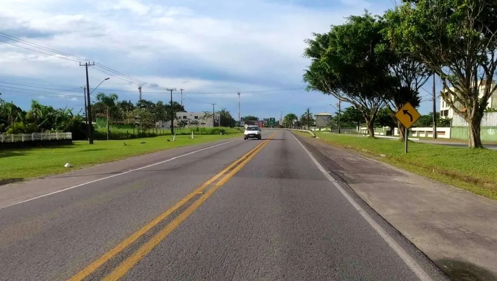 Imagem mostra uma estrada de pista simples com um carro e céu com nuvens.