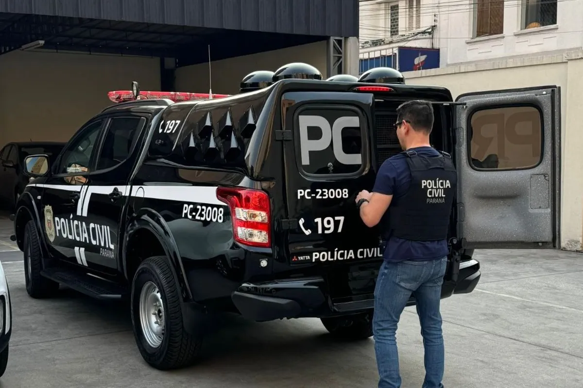 Na imagem, policial aparece em frente à porta traseira de um carro da polícia.