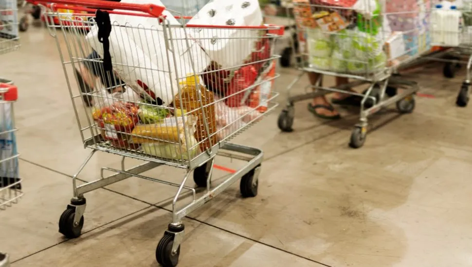 Na imagem, carrinhos com alimentos e outros produtos, dentro de um supermercado.