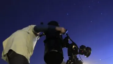 Na imagem, homem observa o céu com um equipamento