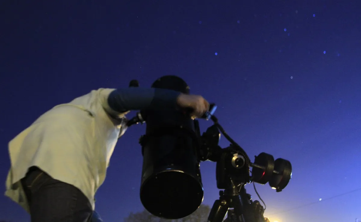 Na imagem, homem observa o céu com um equipamento