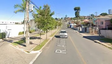 Imagem mostra uma rua de Curitiba, com calçada de um lado e palmeiras em um dia de céu bem azul.