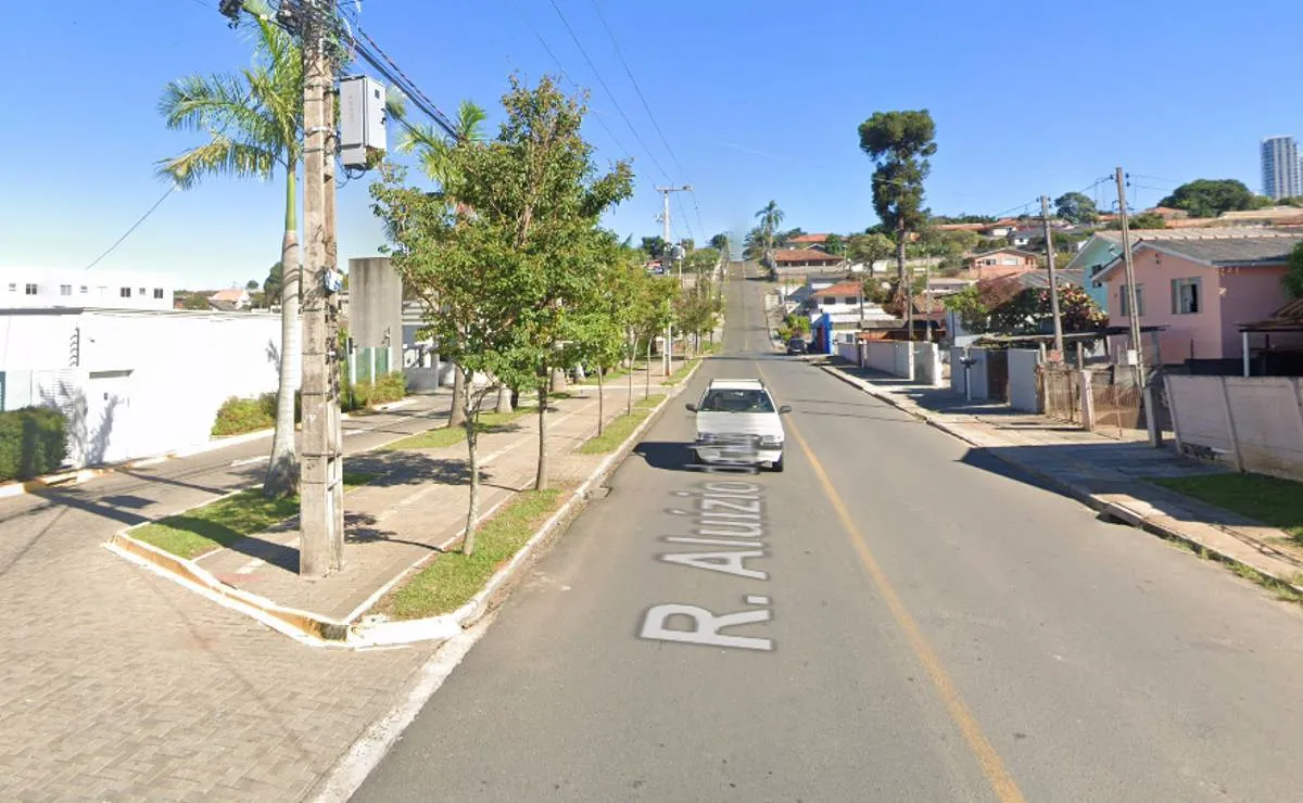 Imagem mostra uma rua de Curitiba, com calçada de um lado e palmeiras em um dia de céu bem azul.