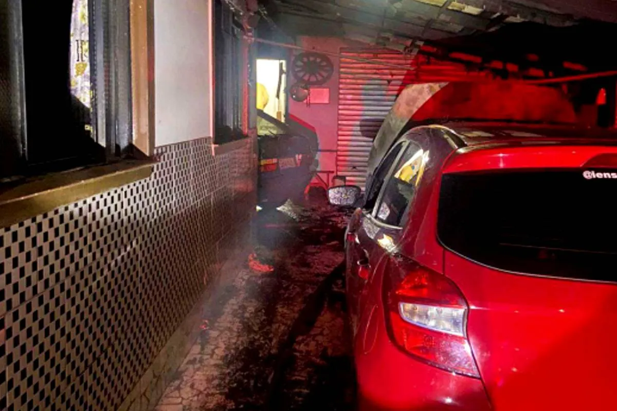 Imagem noturna mostra carros queimados na garagem de uma casa.