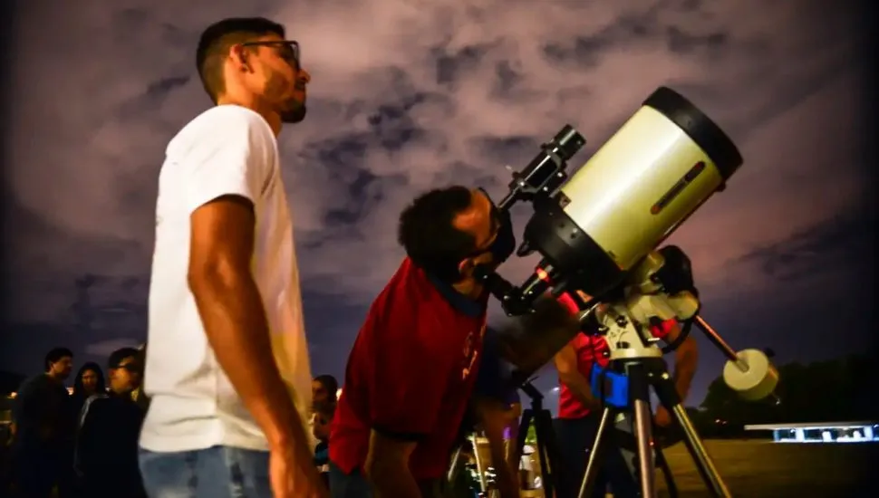 Dois homens jovens observam o céu com a ajuda de um telescópio.