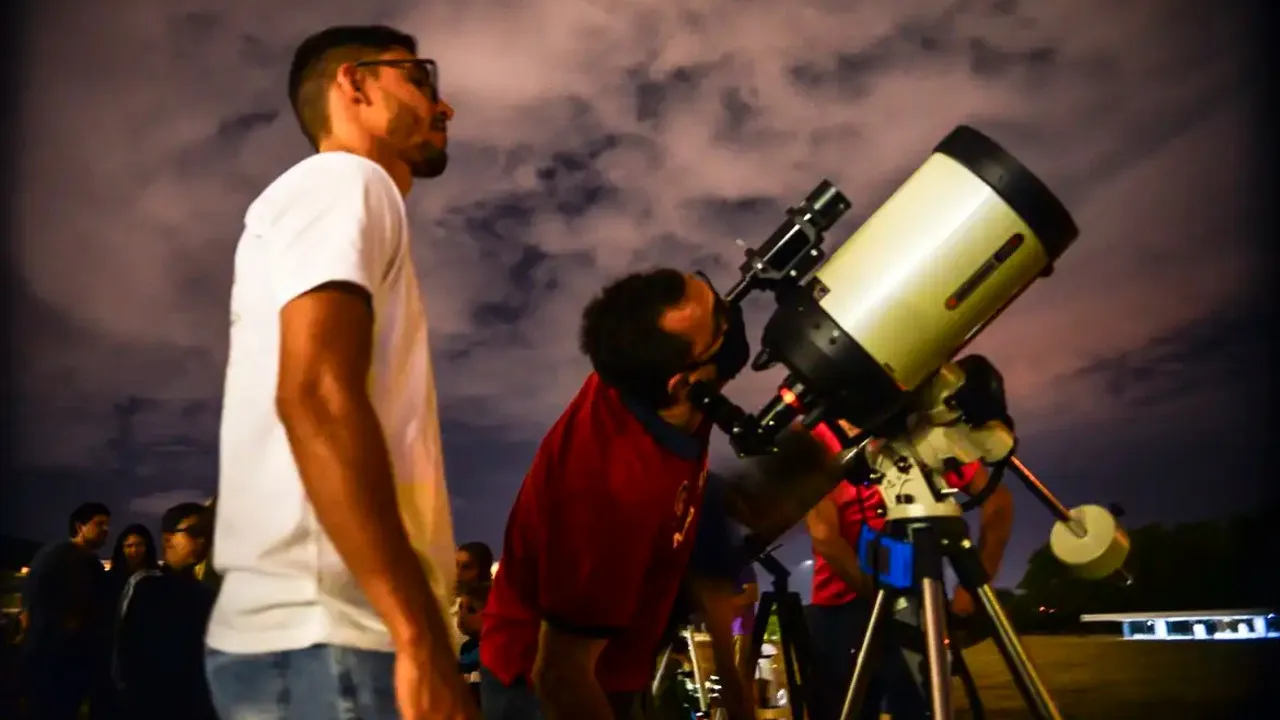 Dois homens jovens observam o céu com a ajuda de um telescópio.