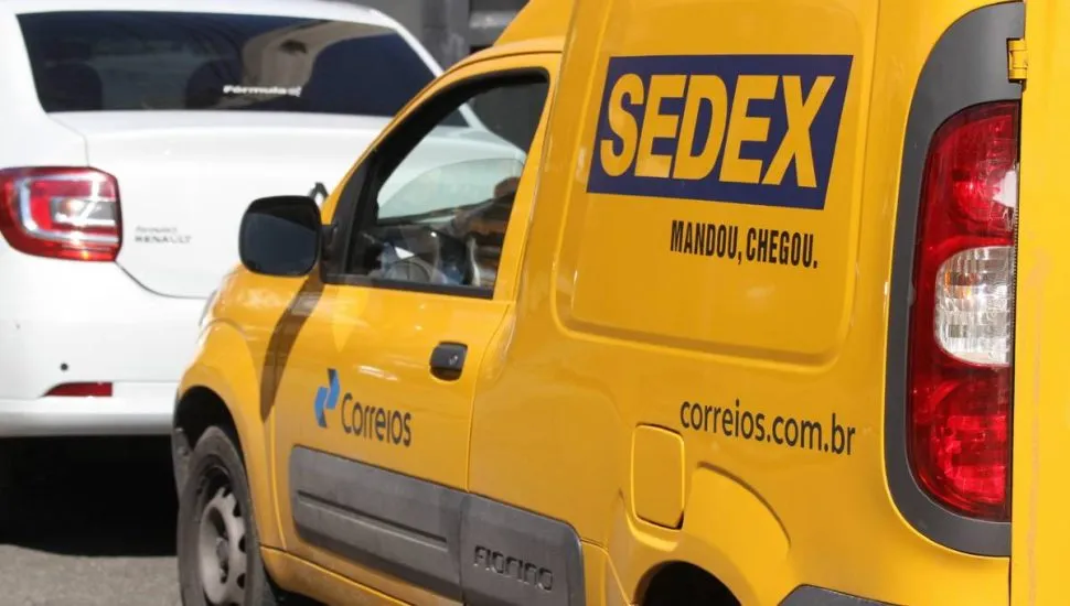 Imagem mostra uma van de entrega dos correios. Tem um carro branco na frente.