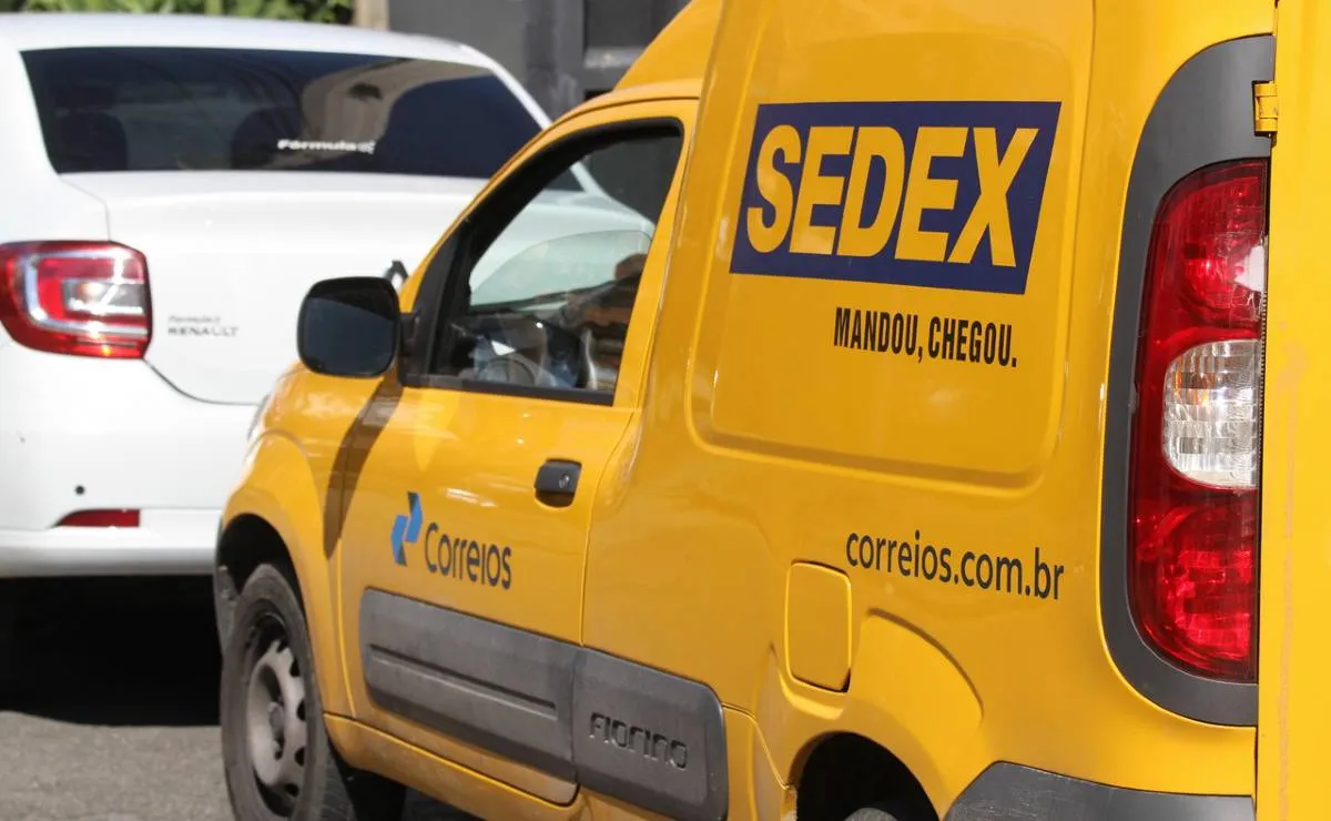 Imagem mostra uma van de entrega dos correios. Tem um carro branco na frente.