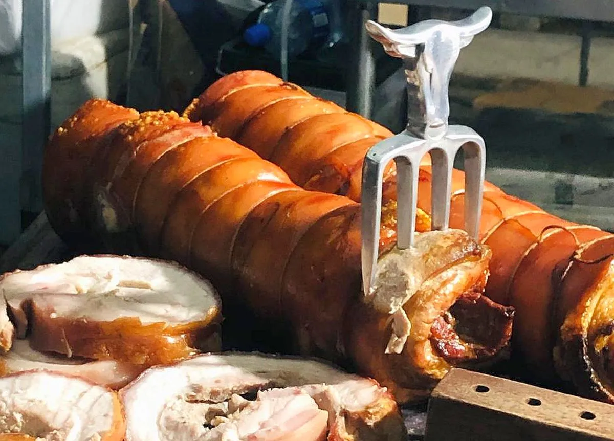 imagem mostra dois pedações grandes de panceta em forma de torresmo de rolo com um carfo espetado.