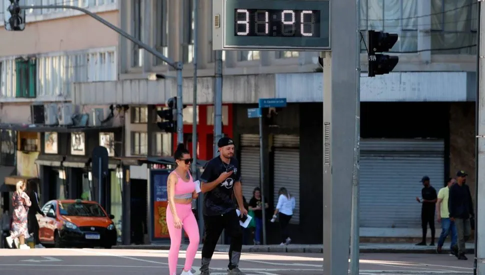 Imagem mostra o centro de Curitiba, com um casal andando em frente a um termômetro de rua com a temperatura de 31ºC