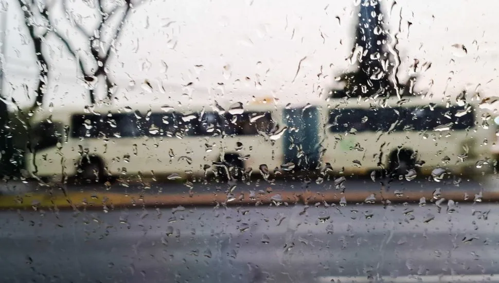 Foto mostra a silueta de um ônibus por detrás de um vidro todo molhado pela chuva