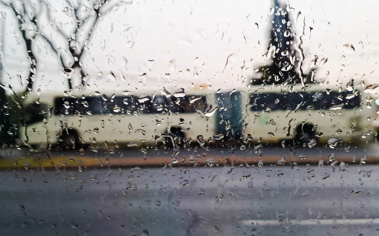 Foto mostra a silueta de um ônibus por detrás de um vidro todo molhado pela chuva