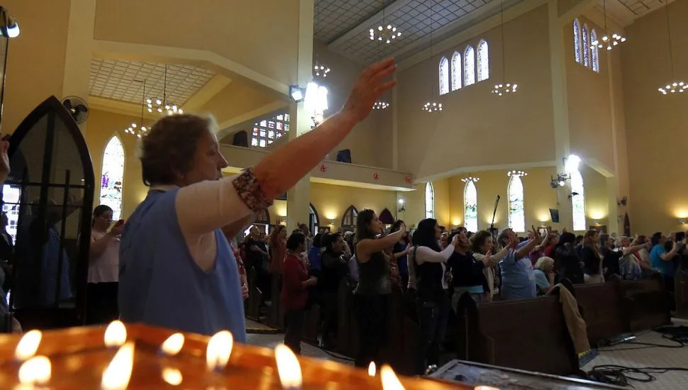 Imagem mostra o salão interno do santuário de Nossa Senhora do Guadalupe, com uma mulher no primeiro plano, fiéis ao fundo e uma mesa de velas em destaque