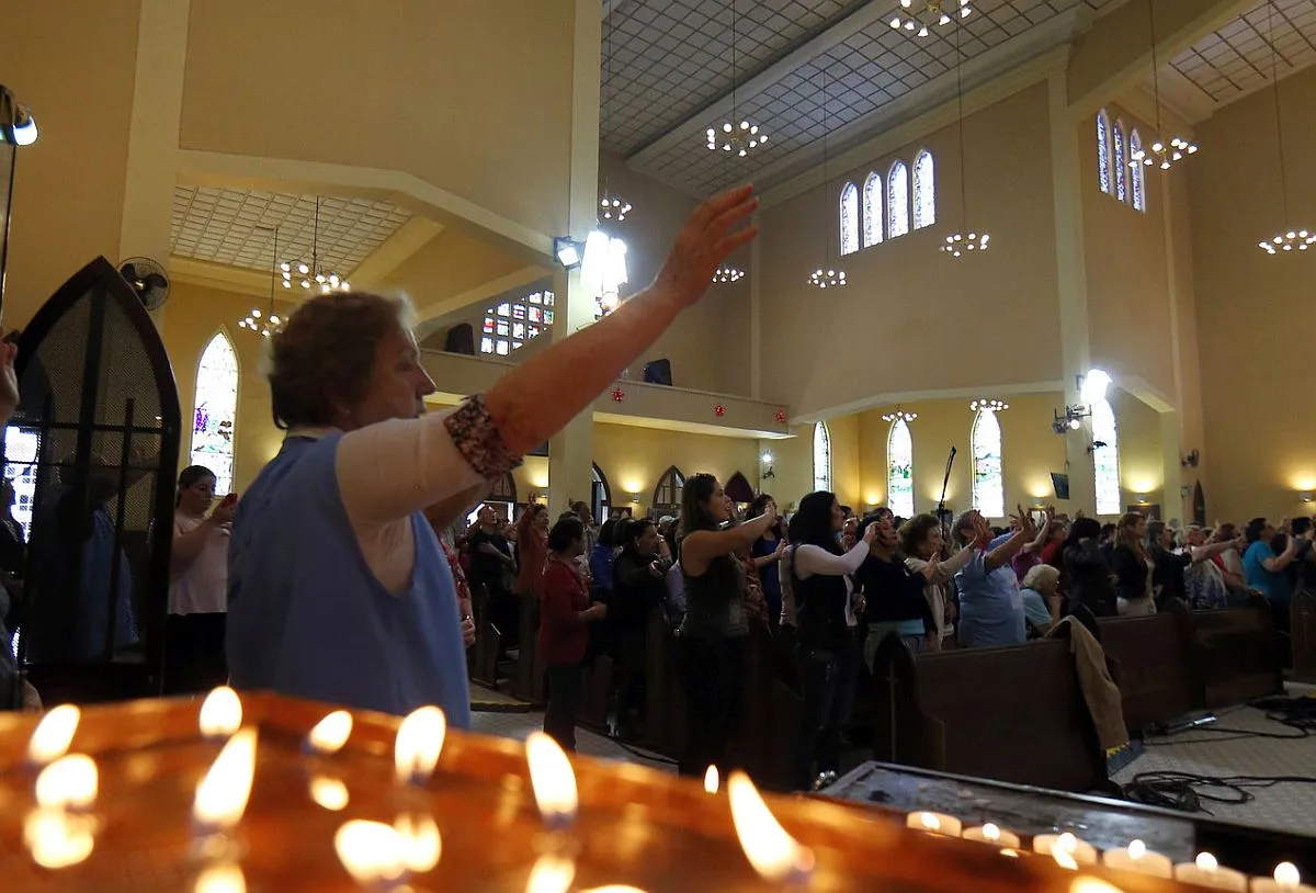 Imagem mostra o salão interno do santuário de Nossa Senhora do Guadalupe, com uma mulher no primeiro plano, fiéis ao fundo e uma mesa de velas em destaque