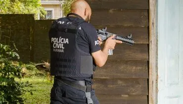 Foto mostra um policial da Polícia Civil segurando uma metralhadora prestes a entrar em um imóvel